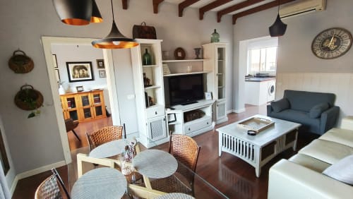 Sala de estar de planta abierta en el hotel Mirador Medieval de Cáceres con mesa de comedor, sofá azul, unidad de TV e iluminación colgante moderna