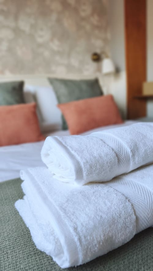 Toallas blancas enrolladas sobre la cama con almohadas coral en el hotel Mirador Medieval de Cáceres