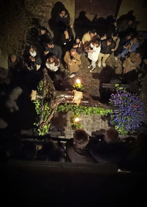 Vigilia nocturna en el Mirador Medieval de Cáceres con multitud reunida alrededor del crucifijo iluminado y flores moradas
