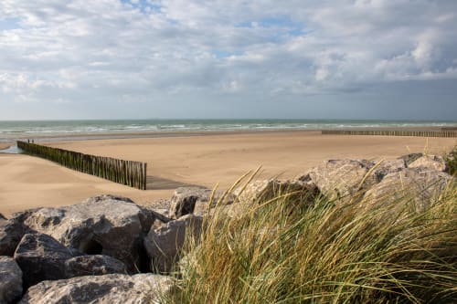 Plage de sable à Ô de Mer à Sangatte avec des épis en bois, rochers côtiers, oyat et ciel nuageux