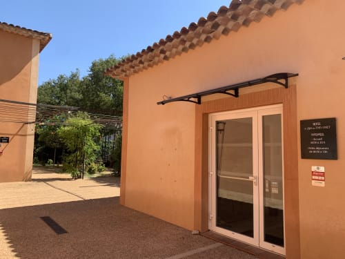 Entrée de l'hôtel Le Clos du Thoronet avec murs en terre cuite, auvent noir et portes vitrées au Thoronet, France