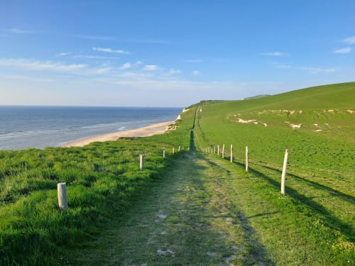 Coastal path with white fence posts overlooking cliffs and beach near Ô de Mer, Sangatte