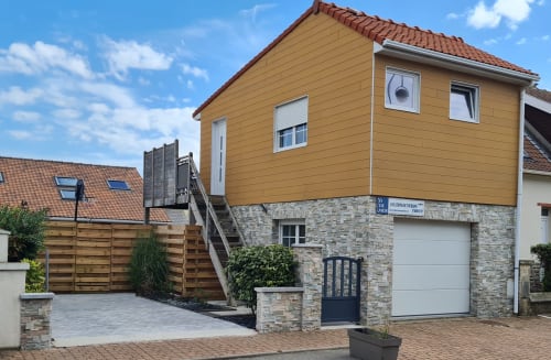 Ô de Mer hotel exterior in Sangatte with yellow-faced upper level, stone foundation, garage, wooden gate, and clear blue sky