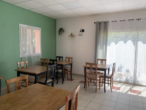 Salle à manger du Clos du Thoronet avec tables et chaises en bois, mur vert, portes vitrées donnant sur le jardin