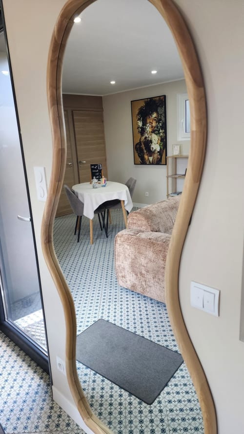 L'entrée de la villa Ô de Mer reflétée dans un miroir à cadre en bois, montrant le séjour avec canapé et table à manger à Sangatte