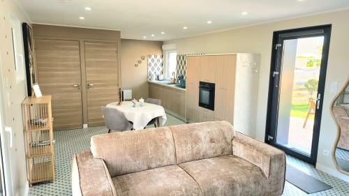 Séjour moderne de la villa Ô de Mer avec canapé beige, cuisine et vue sur le jardin par porte noire, Sangatte