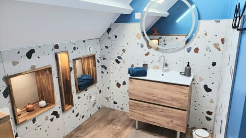 Salle de bain contemporaine de la villa Ô de Mer à Sangatte avec murs en terrazzo, meuble vasque en bois, miroir rond et touches de bleu