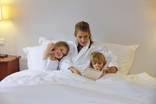 Femme et deux enfants partageant un moment de détente sur le lit de leur chambre à l'Hôtel Louvre Richelieu, Paris