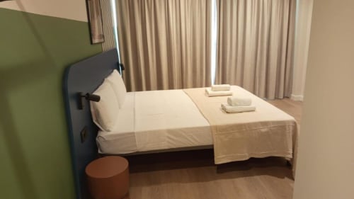 Hostel bedroom at Groma Rooms in Zaragoza with white bedding, blue headboard, and beige curtains