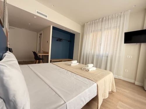 Modern suite at Groma Rooms hostel in Zaragoza with double bed, private bathroom, TV, and large windows