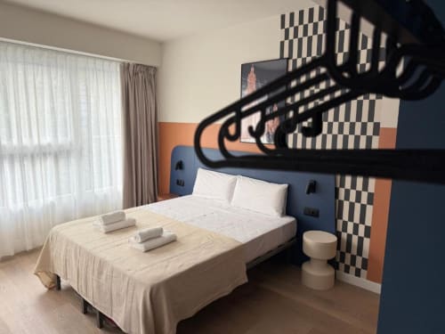Modern hostel room at Groma Rooms in Zaragoza with bunk bed, queen bed, and checkered accent wall design.