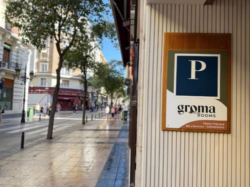 Groma Rooms hostel sign on a Zaragoza street entrance with historic buildings and trees
