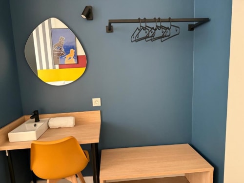 Modern Groma Rooms hostel suite in Zaragoza with blue walls, wooden desk, orange chair, and circular mirror