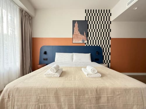 Modern bedroom at Groma Rooms in Zaragoza with blue headboard, beige bedding, and orange accent wall