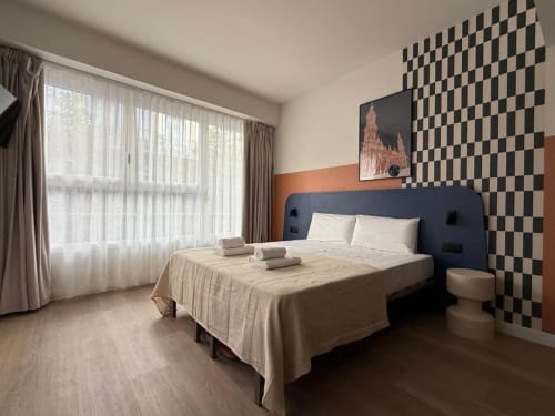 Modern suite at Groma Rooms Zaragoza with blue bed, checkered accent wall, large windows, and private bathroom