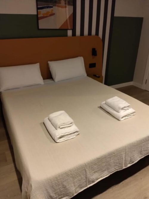 Accessible suite bedroom at Groma Rooms Zaragoza with queen bed, white towels, and orange headboard