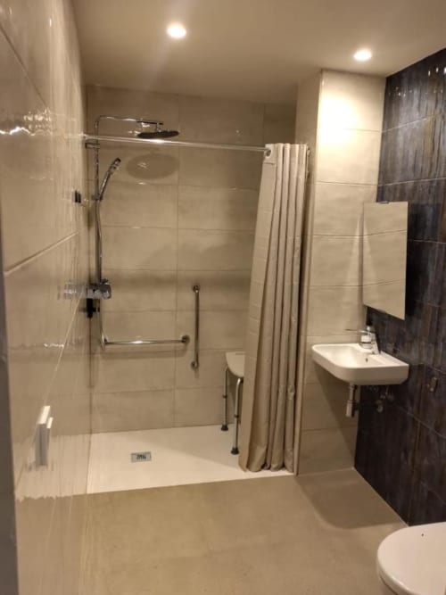 Accessible bathroom at Groma Rooms hostel in Zaragoza with walk-in shower, grab bars, and sink