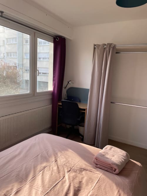 Chambre moderne à Mattbnb Metz avec literie rose, bureau de travail et vue sur la ville par grandes fenêtres