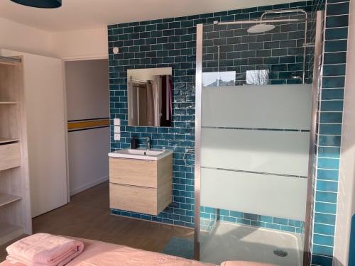 Salle de bain moderne à Mattbnb Metz avec carrelage bleu-vert, vasque en bois, douche ouverte à paroi vitrée dépolie et vue sur la ville