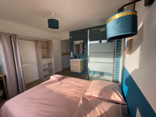 Chambre moderne à Mattbnb Metz avec literie rose, mur en carrelage bleu, salle d'eau, armoire et vue sur la ville