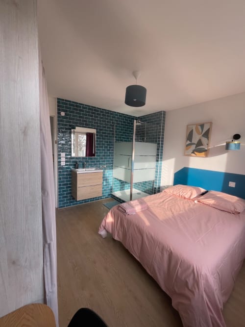 Chambre moderne chez Mattbnb Metz avec literie rose, salle de bain avec douche carrelée turquoise, meuble vasque en bois et coin bureau