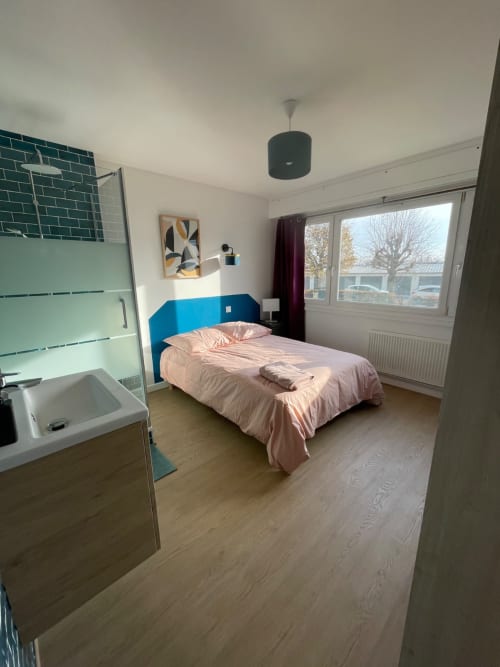 Chambre moderne Mattbnb Metz : tête de lit bleue, literie rose, salle de douche privée, bureau et vue sur la ville