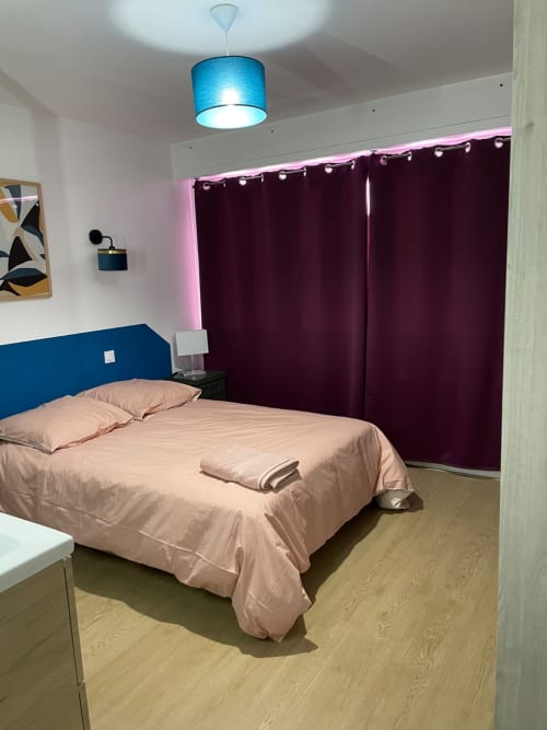 Chambre moderne chez Mattbnb Metz avec tête de lit bleue, literie rose, rideaux violets et lustre bleu