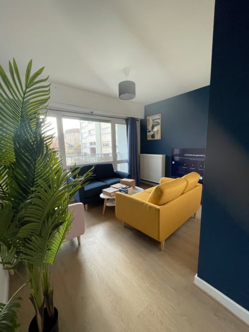 Salon moderne à Mattbnb Metz avec fauteuil jaune, canapé bleu et balcon vue ville