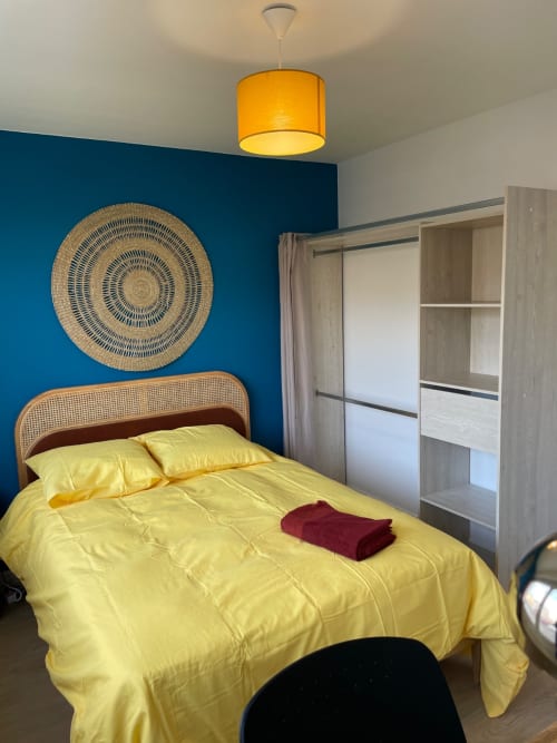 Bright yellow bedroom with teal accent wall, rattan circular art, and wardrobe at Mattbnb hotel in Metz