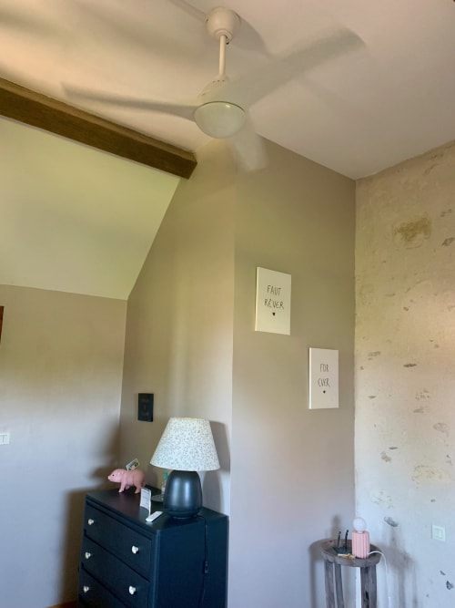 Chambre taupe avec ventilateur de plafond crème, commode noire avec lampe et art mural inspirant au Logis de la chouette B&B