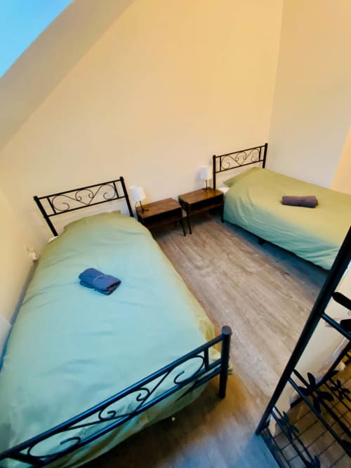 Deux lits simples avec têtes de lit en fer forgé et linge de lit bleu dans une chambre lumineuse de Business Apparts Caudry
