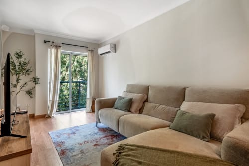 Sala de estar luminosa em Atlantic Places Albufeira com sofá bege, vista para o jardim e comodidades modernas