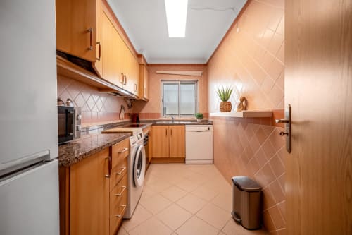Cozinha moderna com armários de madeira, revestimento de azulejos de terracota e eletrodomésticos em aço inoxidável no Atlantic Places, Albufeira