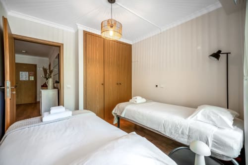 Quarto duplo luminoso na Atlantic Places Albufeira com guarda-roupas em madeira, luminária pendente e moderno candeeiro de pé preto
