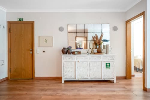 Entrada luminosa do apartamento The Quiet Nest em Atlantic Places, Albufeira, com portas de madeira, móvel branco e vista para o jardim