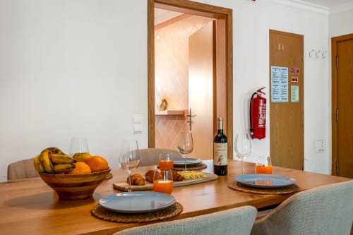 Sala de jantar do apartamento The Quiet Nest em Atlantic Places, Albufeira com mesa de madeira, talheres, garrafa de vinho e fruta