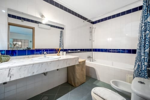 Banheiro moderno em Atlantic Places Albufeira com bancada em mármore, detalhes em azulejo azul, banheira e janela com vista para o jardim