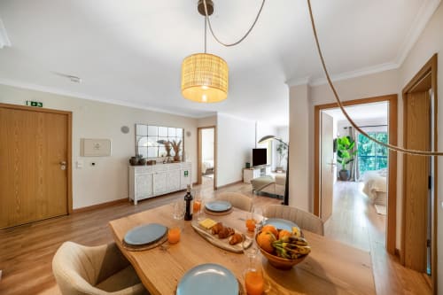 Sala de refeições luminosa com mesa de madeira, janelas com vista para o jardim e mobiliário moderno em Atlantic Places, Albufeira