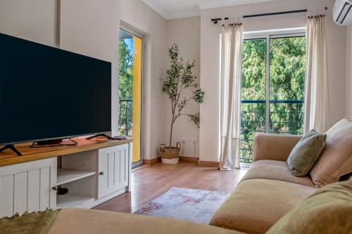 Sala de estar luminosa em Albufeira com vista para o jardim, TV moderna, sofá bege e planta em vaso
