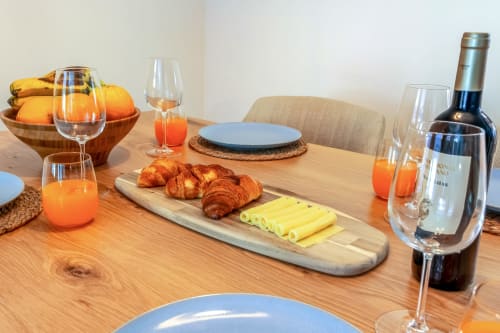 Mesa de café da manhã elegante no Atlantic Places Albufeira com croissants, queijo, suco fresco, vinho e pratos azuis