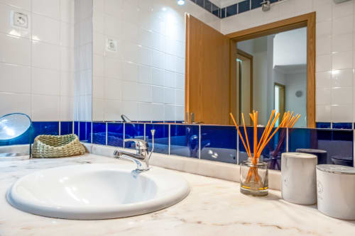 Banheiro moderno no apartamento The Quiet Nest em Atlantic Places, Albufeira, com lavatório branco, detalhes em azulejo azul e acabamentos em madeira