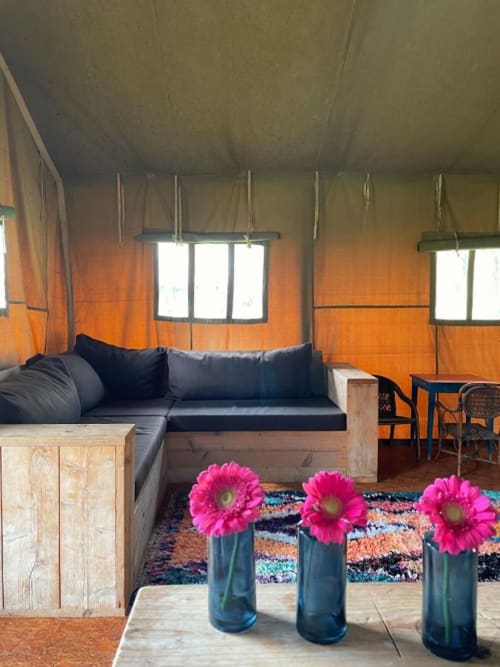 Intérieur cosy du glamping Les gîtes de Cormenin avec canapé noir, murs orange, fleurs roses et lumière naturelle