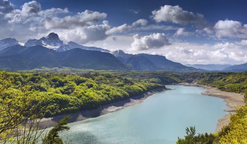 Lac turquoise entouré de forêt verte avec montagnes enneigées à Corps, France, près de l'Hôtel le Tilleul