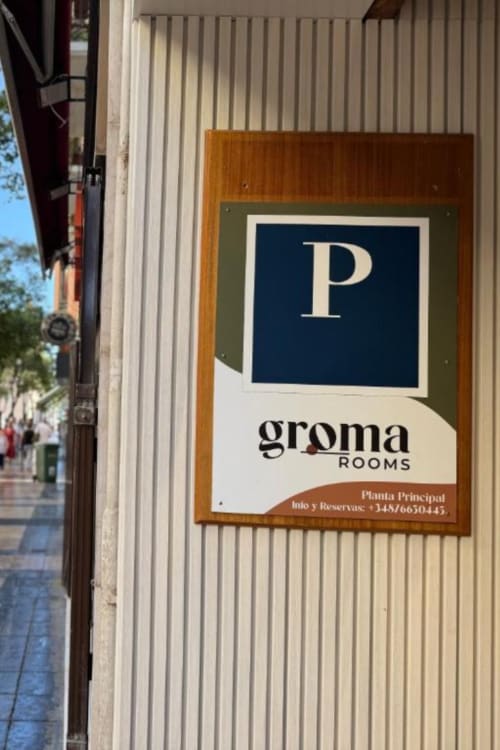 Groma Rooms hostel sign in Zaragoza with blue 'P' logo on wooden frame against corrugated metal wall