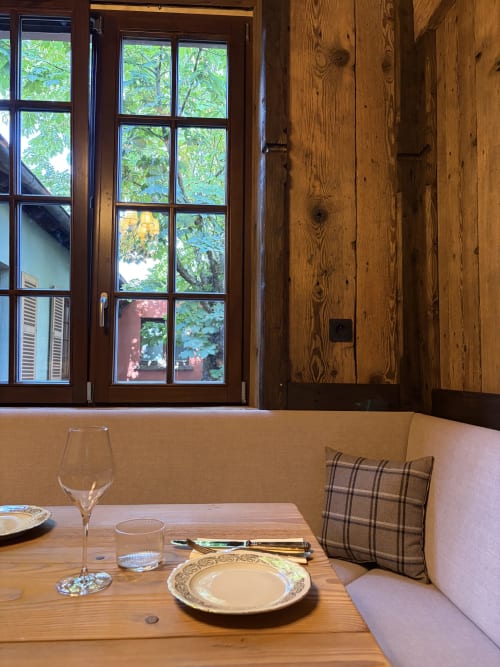 Coin repas à l'Hôtel l'Ange à Niedermorschwihr avec table en bois, couvert dressé et vue sur la verdure par de grandes fenêtres