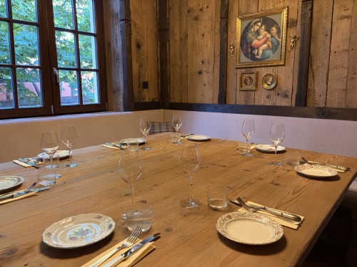 Salle à manger élégante de l'Hôtel l'Ange avec table en bois, couverts, verres à vin et œuvres d'art classiques