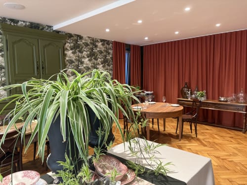 Élégante salle à manger de l'Hôtel l'Ange à Niedermorschwihr avec plante verte, table en bois, rideaux rouges et décor classique.