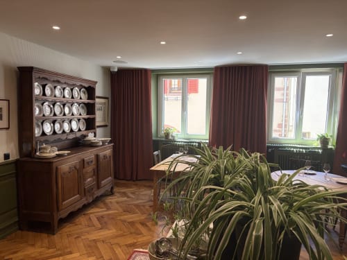 Élégante salle à manger de l'hôtel l'Ange à Niedermorschwihr avec buffet en bois, rideaux bordeaux et parquet en chevrons