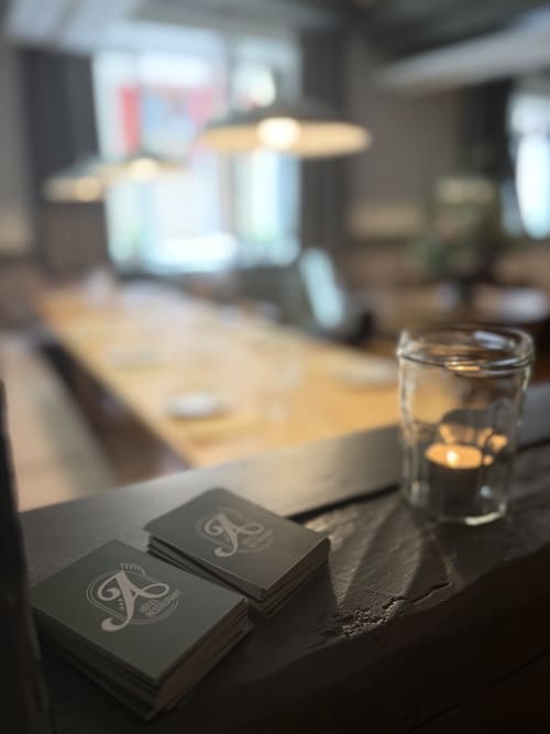 Cartes de visite noires avec logo sur surface sombre, à côté d'une bougie allumée à l'Hôtel-Restaurant l'Ange de Niedermorschwihr