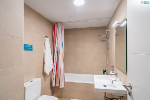 Baño moderno en Alhaurín Loft con azulejos beige, lavamanos blanco, espejo, bañera y cortina a rayas
